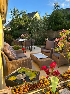 An outdoor patio area with wicker furniture, a table, and a small water feature. - Bed and Breakfast 'Escale Sabolienne' with Shared Garden and Wi-Fi (Sablé-sur-Sarthe)