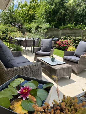 An outdoor patio with wicker furniture, a table, and a flower pond. - Bed and Breakfast 'Escale Sabolienne' with Shared Garden and Wi-Fi (Sablé-sur-Sarthe)