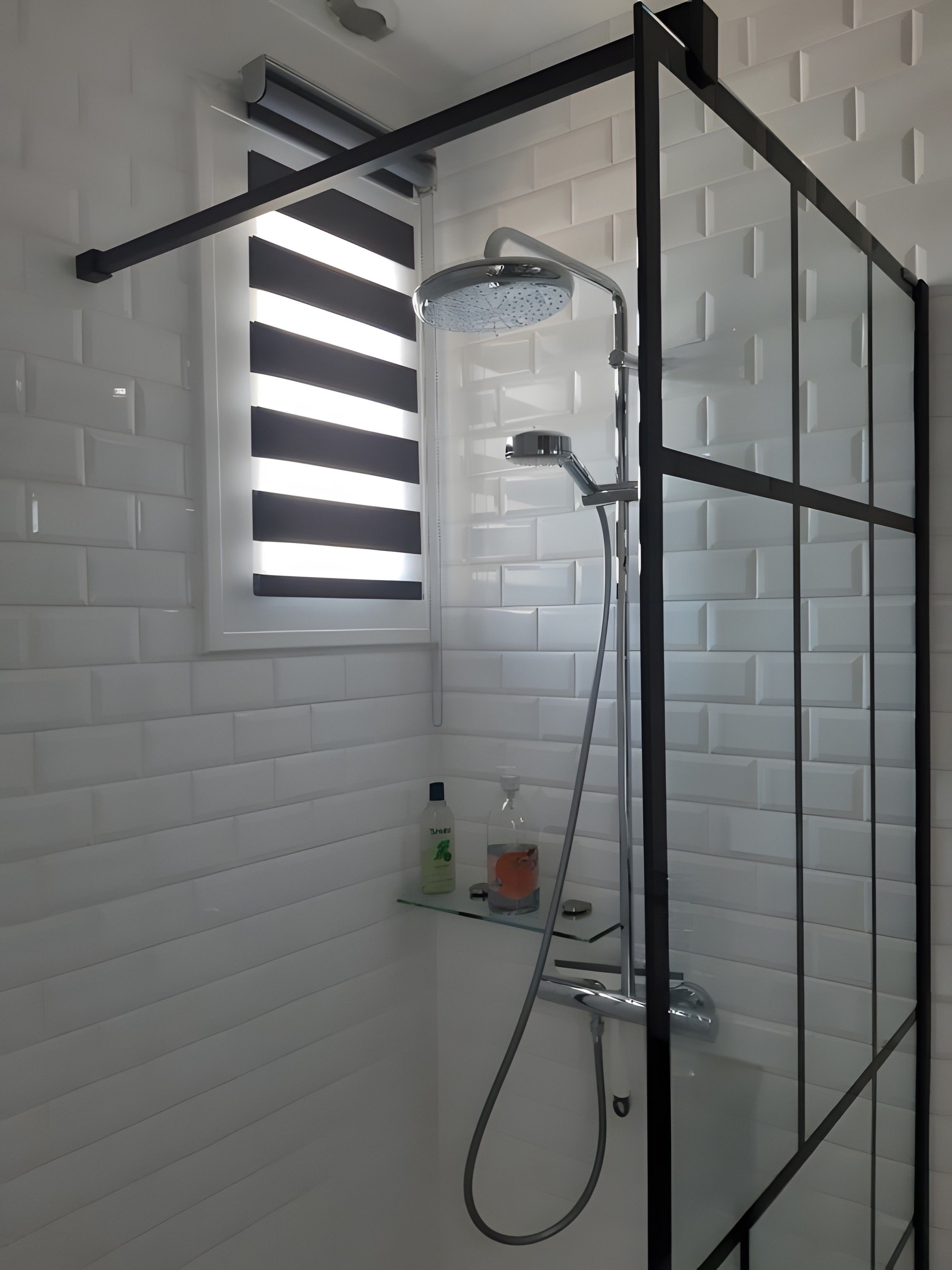 Une cabine de douche moderne dotée d’une porte en verre, d’un pommeau de douche à main et d’une petite étagère pour les articles de toilette.