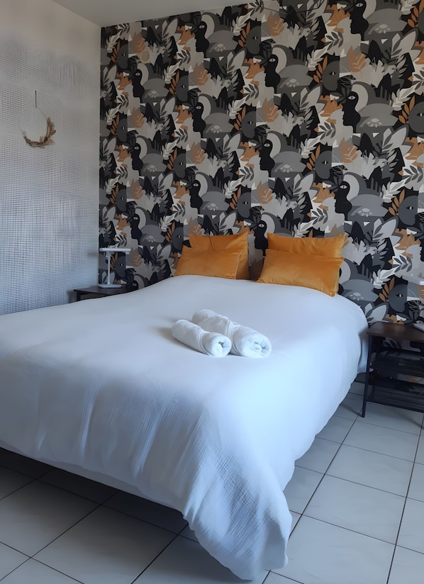 Una cama bien hecha con sábanas blancas y toallas enrolladas, un papel tapiz estampado con diseños abstractos y un adorno de pared con textura.