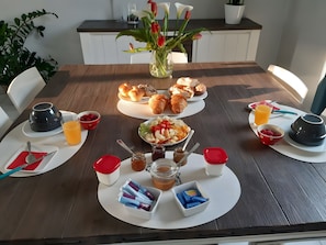 Una mesa de desayuno lista con cruasanes, muffins, fruta y salsas.