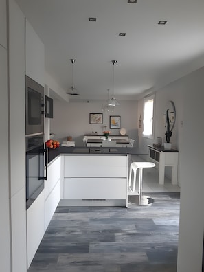 Una cocina moderna con una isla central, iluminación colgante y un comedor.