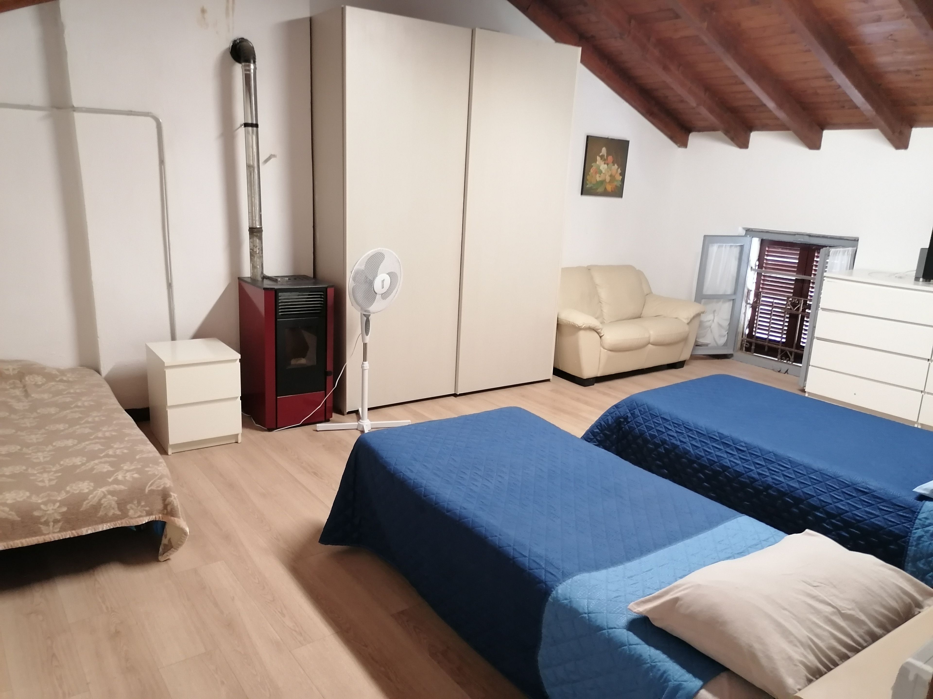 Un dormitorio con dos camas, un calentador, un ventilador, un armario y una silla.
