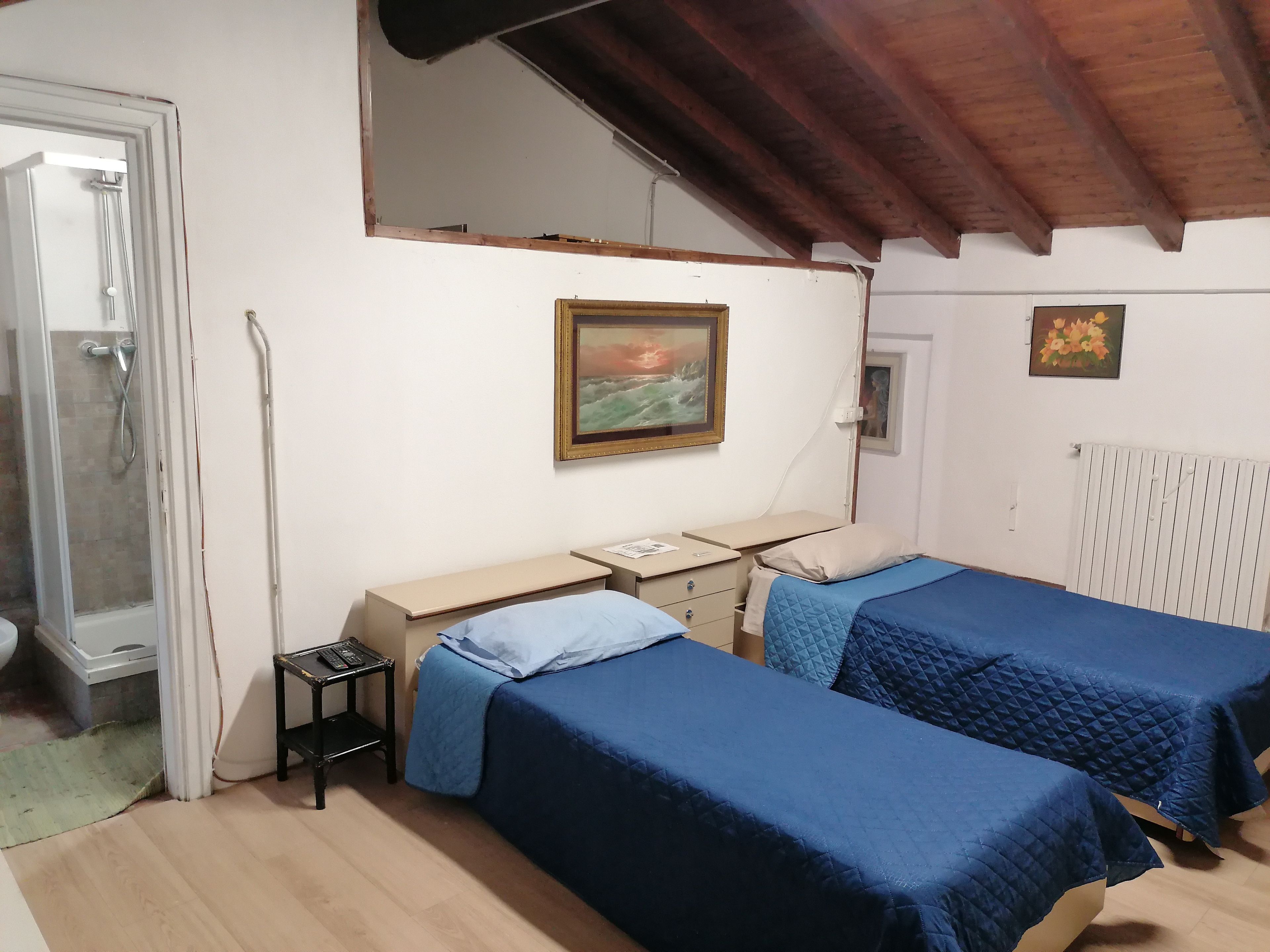 A bedroom with two beds, a desk, a chair, a radiator, and a painting on the wall.