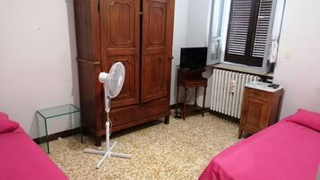 Un dormitorio con un armario de madera, un ventilador de pie, un radiador, un televisor y dos camas con cubrecamas rosas.