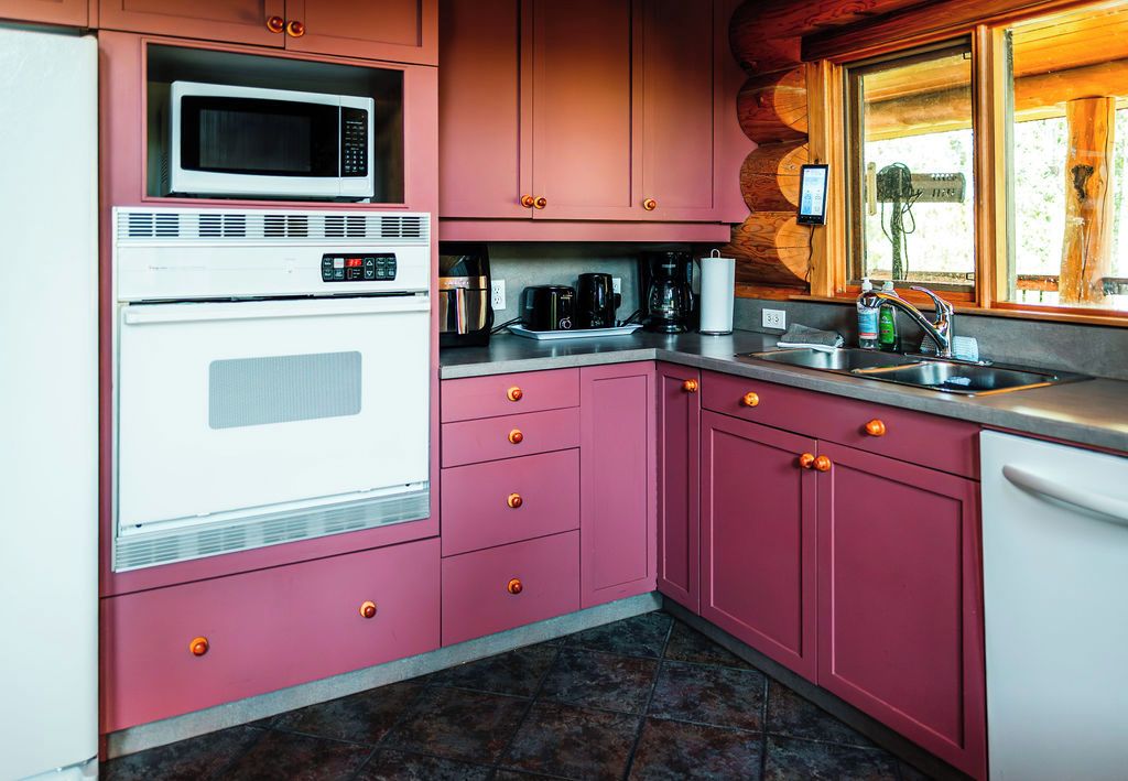 Uma cozinha com armários rosa, micro-ondas, forno, cafeteira e pia.