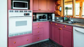 Uma cozinha com armários rosa, micro-ondas, forno, cafeteira e pia.