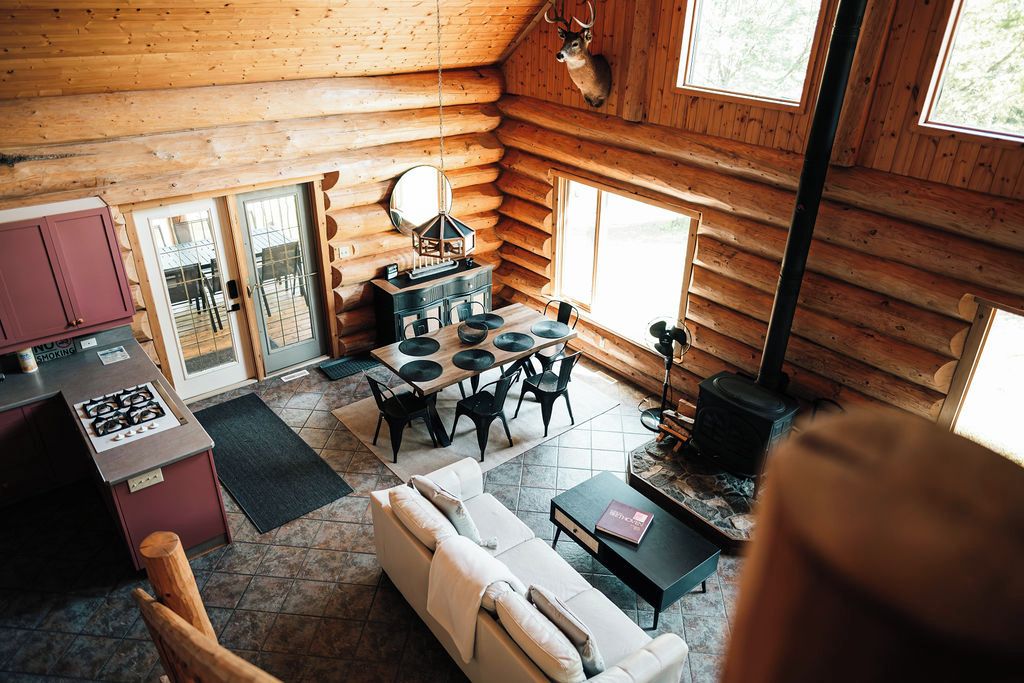 Interior de cabana de toras com sala de jantar, sofá e lareira.