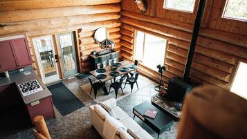 Interior de cabana de toras com sala de jantar, sofá e lareira.