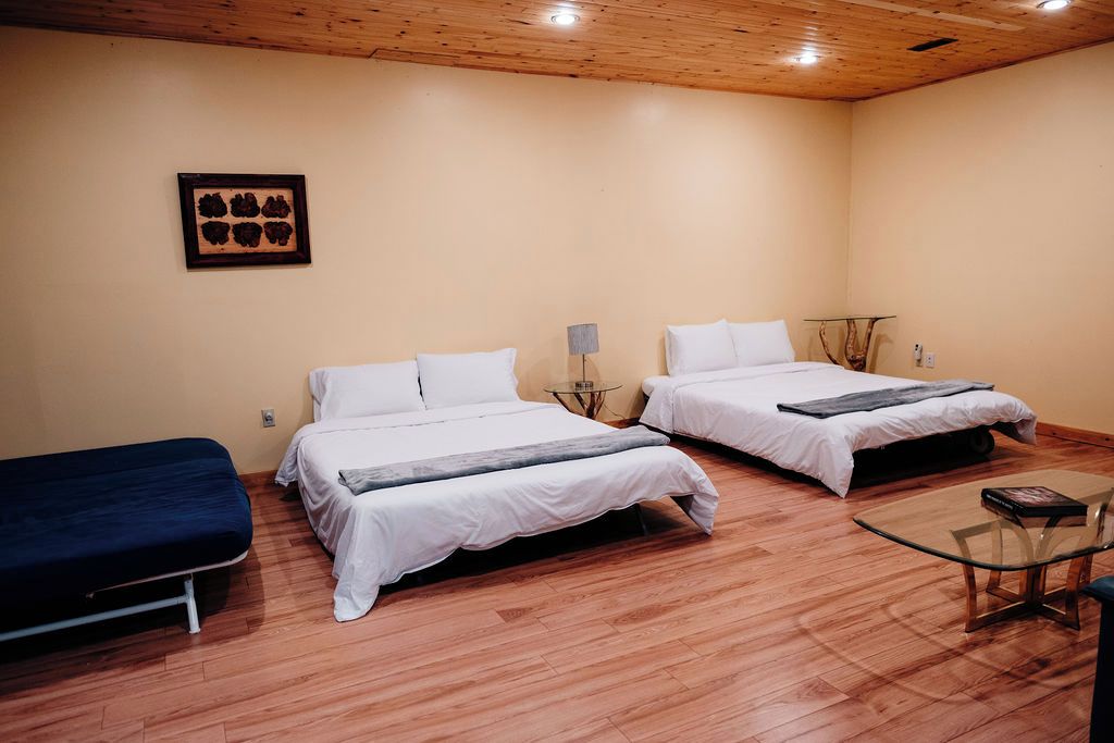 A room with two beds, a small table, and a wall-mounted picture.