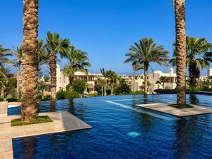 Schwimmbeckenbereich eines Resorts mit Palmen und blauem Himmel.