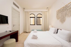 A hotel room with a bed, a desk, a television, and a window with curtains. - VESTA - Luxury APT - 1BR - Ancient sands (El Gouna)