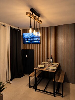 A dining area with a wooden table, black metal frame, and a flat-screen TV mounted on the wall. - Châtel - Charming, renovated apartment with a balcony offering mountain views - Sleeps 4 (chatel)