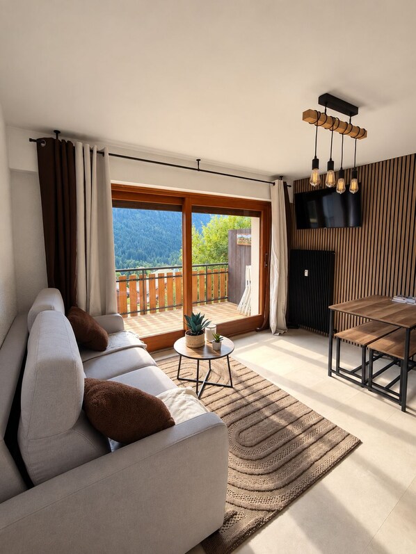 A modern living room with a sofa, a small round table, and a dining table. - Châtel - Charming, renovated apartment with a balcony offering mountain views - Sleeps 4 (chatel)