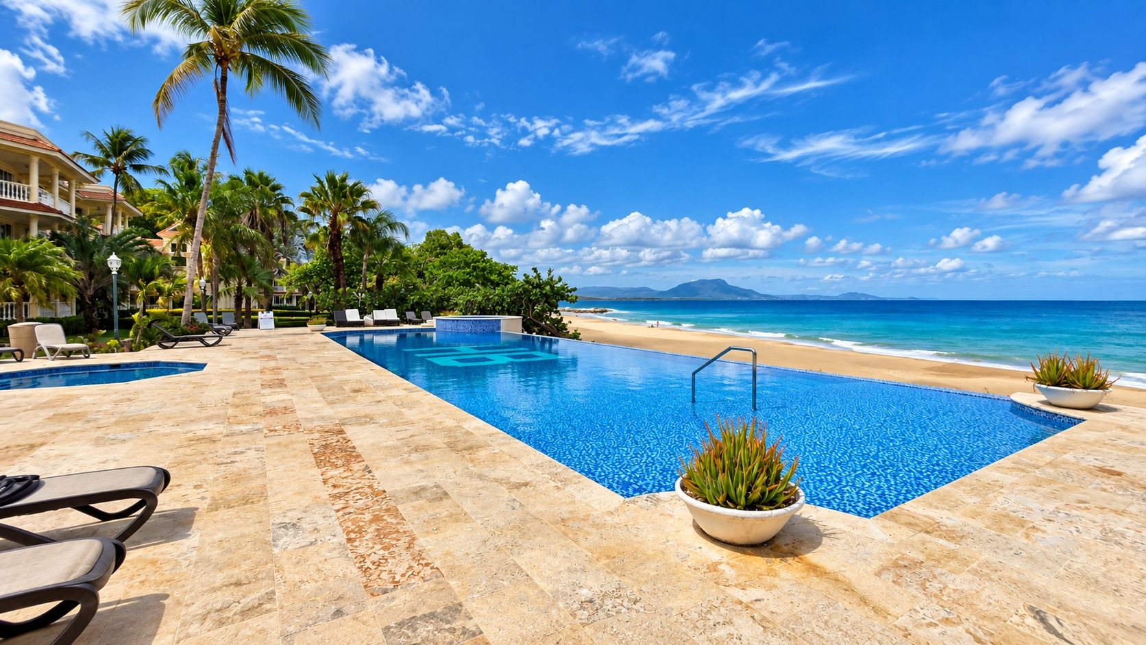 A pool area with a view of the beach and ocean, surrounded by palm trees and lounge chairs.