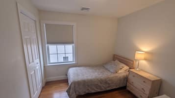 Un dormitorio pequeño con una cama individual, una mesita de noche, una lámpara y una ventana con persianas.