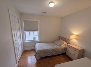 Un dormitorio pequeño con una cama individual, una mesita de noche, una lámpara y una ventana con persianas.