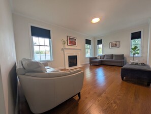 Una sala de estar con chimenea, un sofá gris, un sofá seccional y un otoman oscuro.