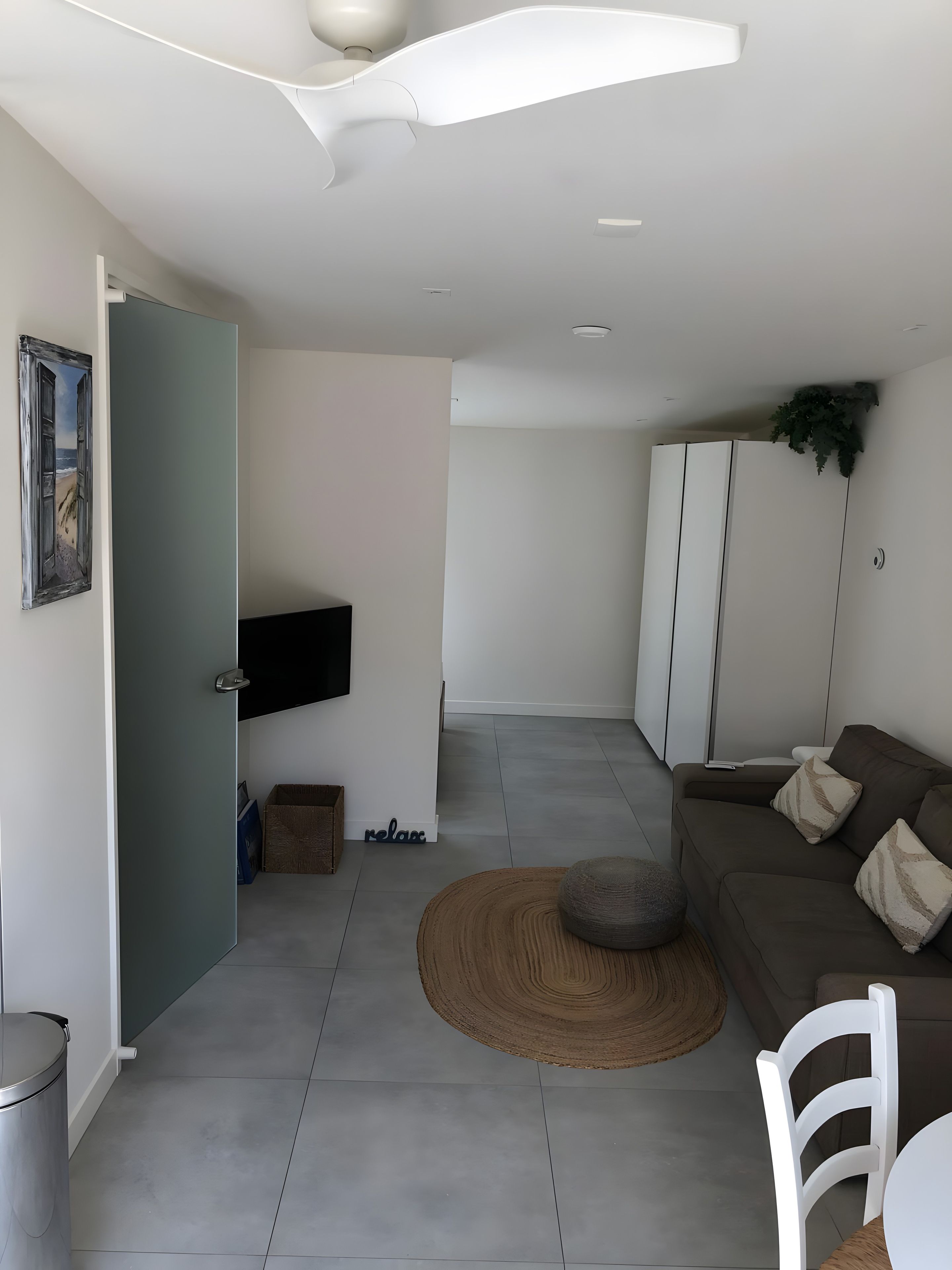 A modern living room with a sofa, a round rug, a white chair, and a television mounted on the wall.