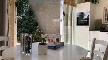 A modern kitchen with a built-in oven, a dining table with chairs, and a view of a brick wall and greenery outside.