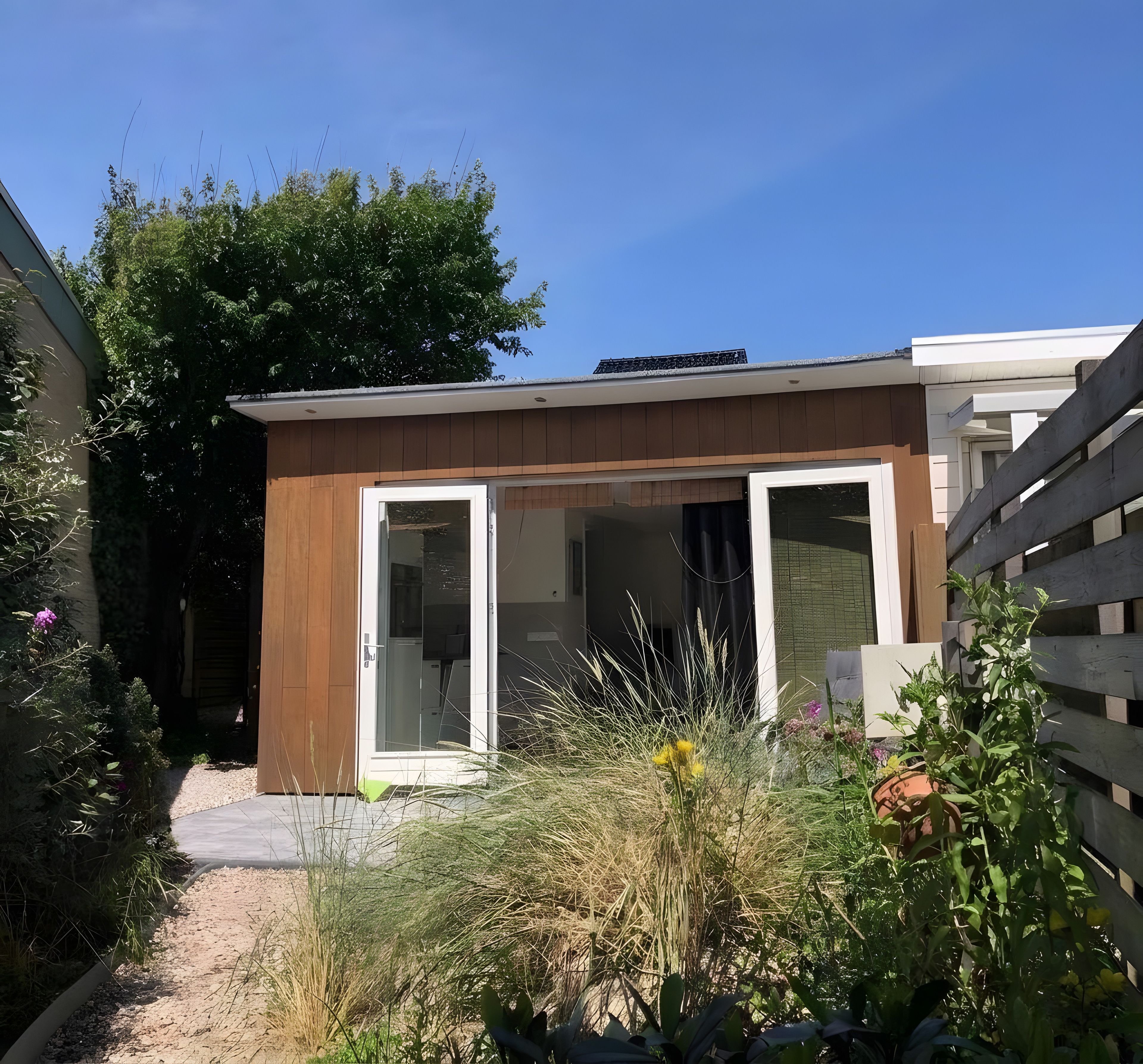 A modern house with a wooden exterior, a glass door entrance, and a gravel pathway leading to the door.