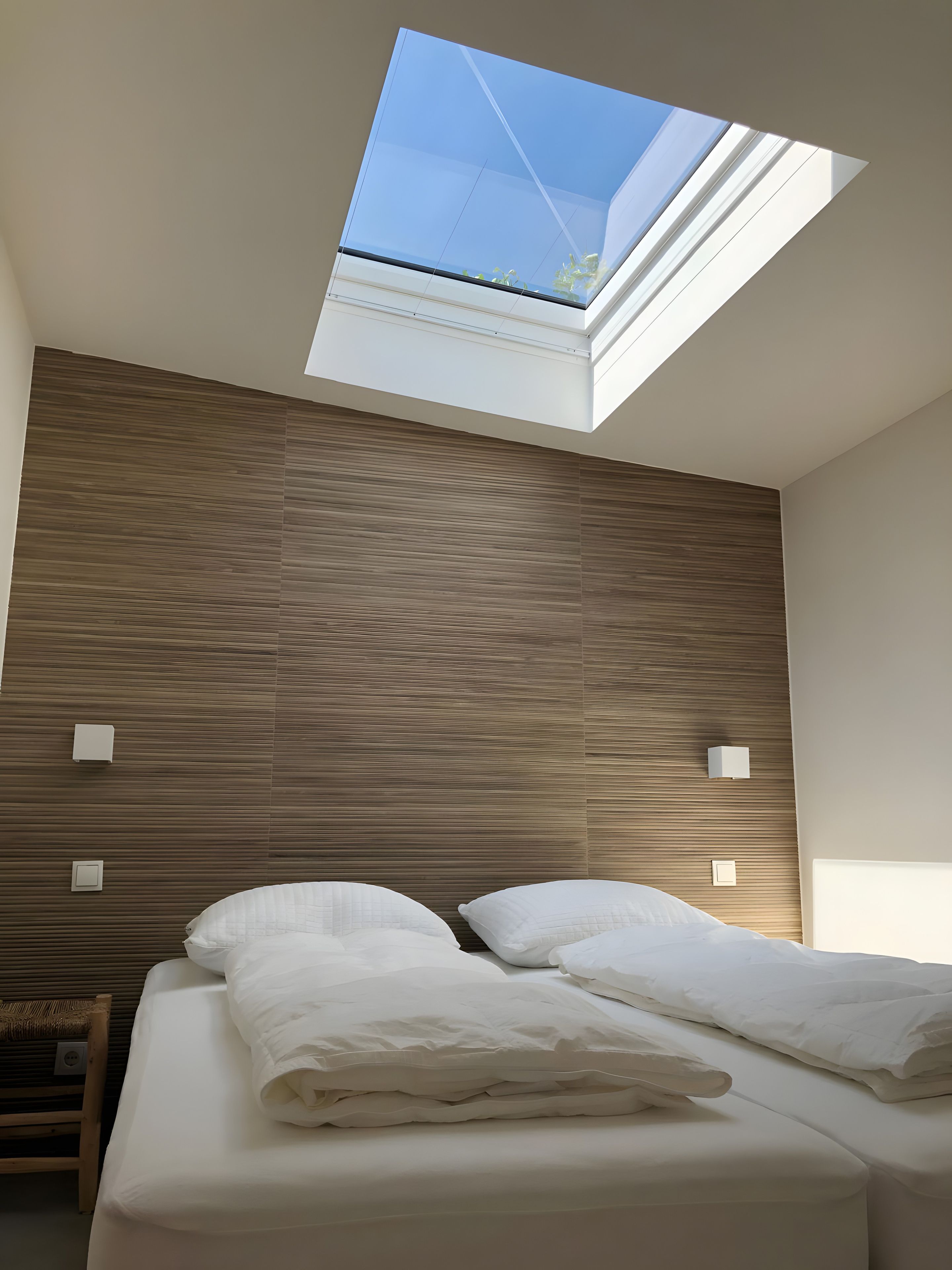 A modern bedroom with a skylight, wooden panel wall, and a bed with white linens.