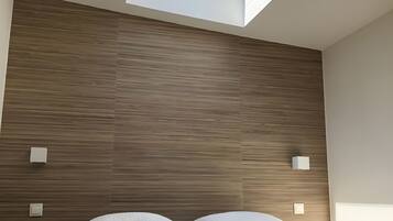 A modern bedroom with a skylight, wooden panel wall, and a bed with white linens.