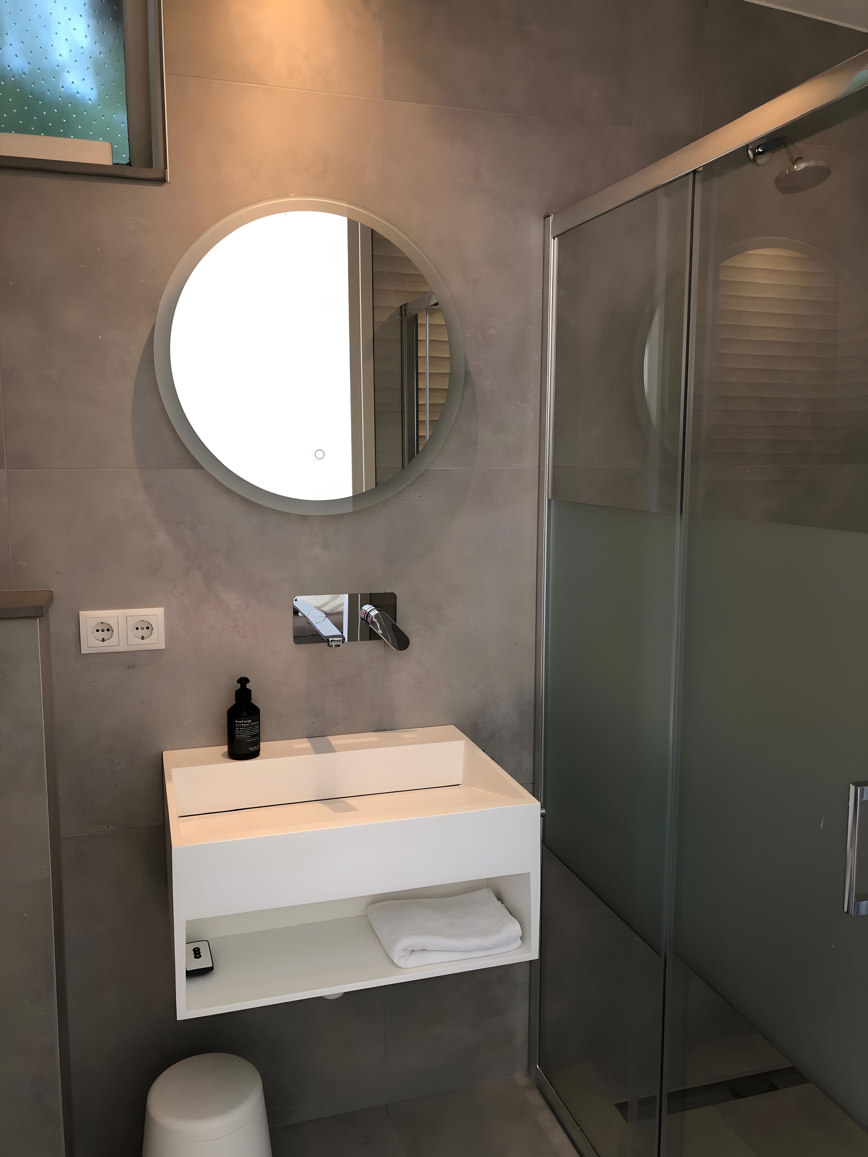 A modern bathroom with a round mirror, a white sink, and a glass shower enclosure.