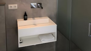 Ein modernes Badezimmer mit rundem Spiegel, Waschbecken in Weiß und einer Duschkabine aus Glas.