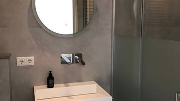 A modern bathroom with a round mirror, a white sink, and a glass shower enclosure.