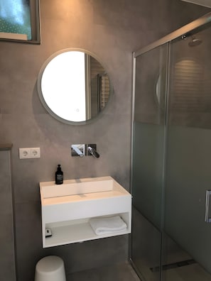 Ein modernes Badezimmer mit rundem Spiegel, Waschbecken in Weiß und einer Duschkabine aus Glas.