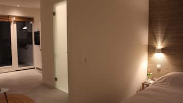 Une chambre d’hôtel moderne, équipée d’un lit, d’une petite table de chevet, d’une commode et d’un luminaire fixé au mur.