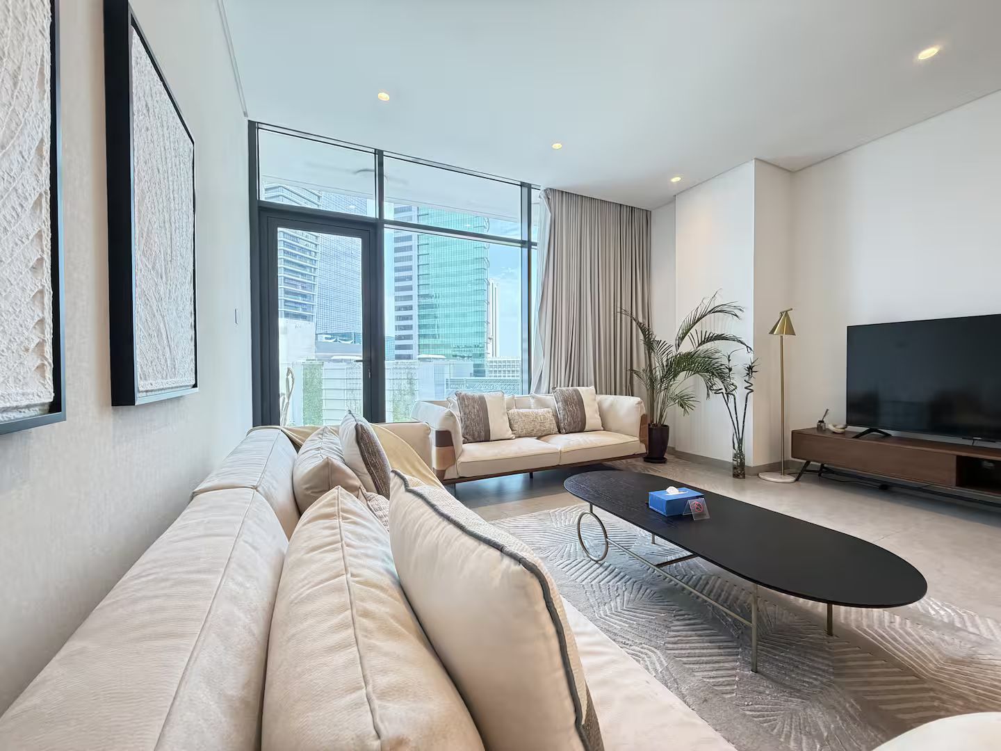 Ein modernes Wohnzimmer mit einer Couch, einem Couchtisch, einem Fernseher und einem großen Fenster mit Blick auf die Stadt.