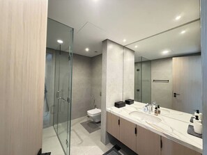 Een moderne badkamer met een douchecabine van glas, een toilet en een wastafelmeubel met een wastafel en spiegel.