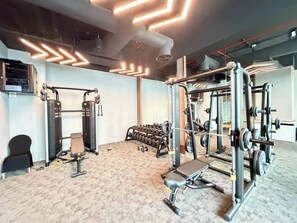 Een fitnessruimte met diverse trainingsapparaten, waaronder een squatraam, bankdrukapparaat en gewichten.