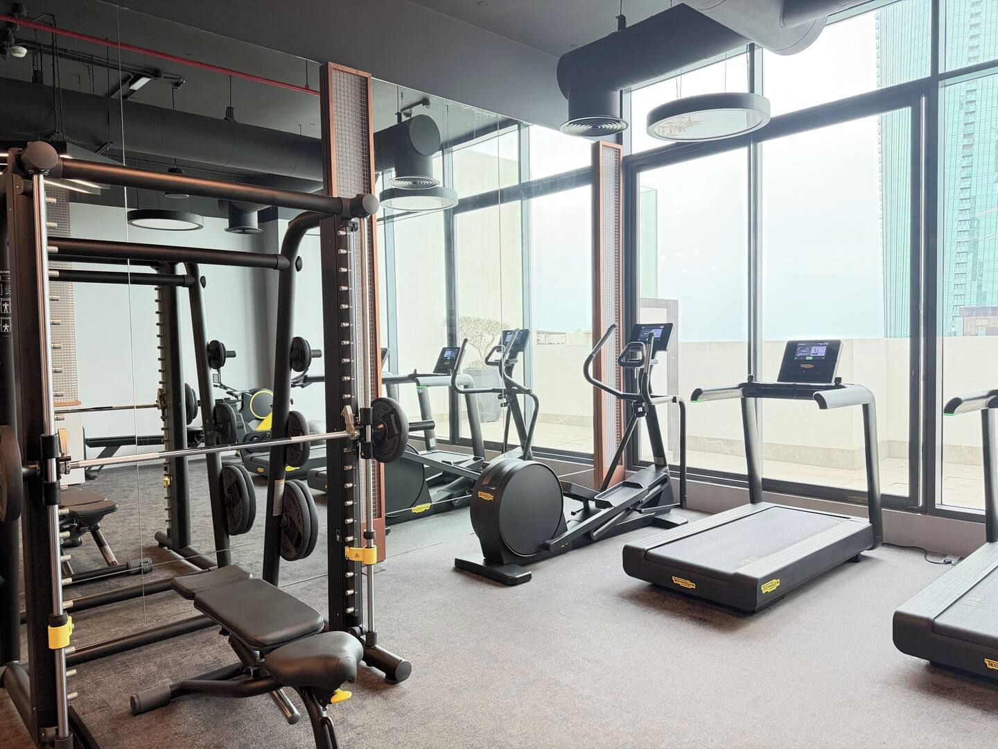 Een sportschool met trainingsapparatuur, een bank en grote ramen met uitzicht op de stad.