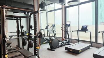 Een sportschool met trainingsapparatuur, een bank en grote ramen met uitzicht op de stad.