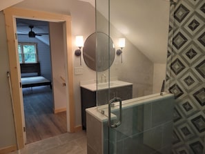 Une salle de bain avec une douche à parois de verre, un lavabo avec un miroir et un ventilateur de plafond.