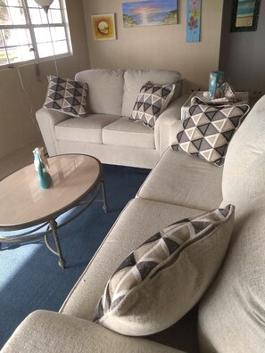 Ein Wohnzimmer mit einem beigefarbenen Sofa, gemusterten Kissen, einem kleinen runden Tisch und einer dekorativen Vase.