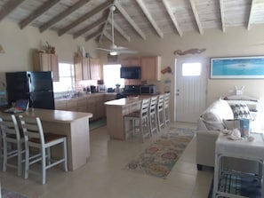 A kitchen with a central island, dining area with chairs, a refrigerator, and a microwave. - Rainbow Bay, MERMAIDS Cozy 2-bedroom house Ocean Front short walk to 5 Beaches (Eleuthera)