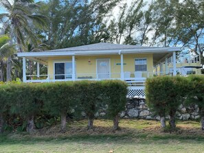 A two-story house with a covered porch, a stone wall, and a grassy lawn. - Rainbow Bay, MERMAIDS Cozy 2-bedroom house Ocean Front short walk to 5 Beaches (Eleuthera)