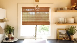 Eine Küche mit Fenster, Spüle, Schränken und einem Regal mit Geschirr und einem Vogel.