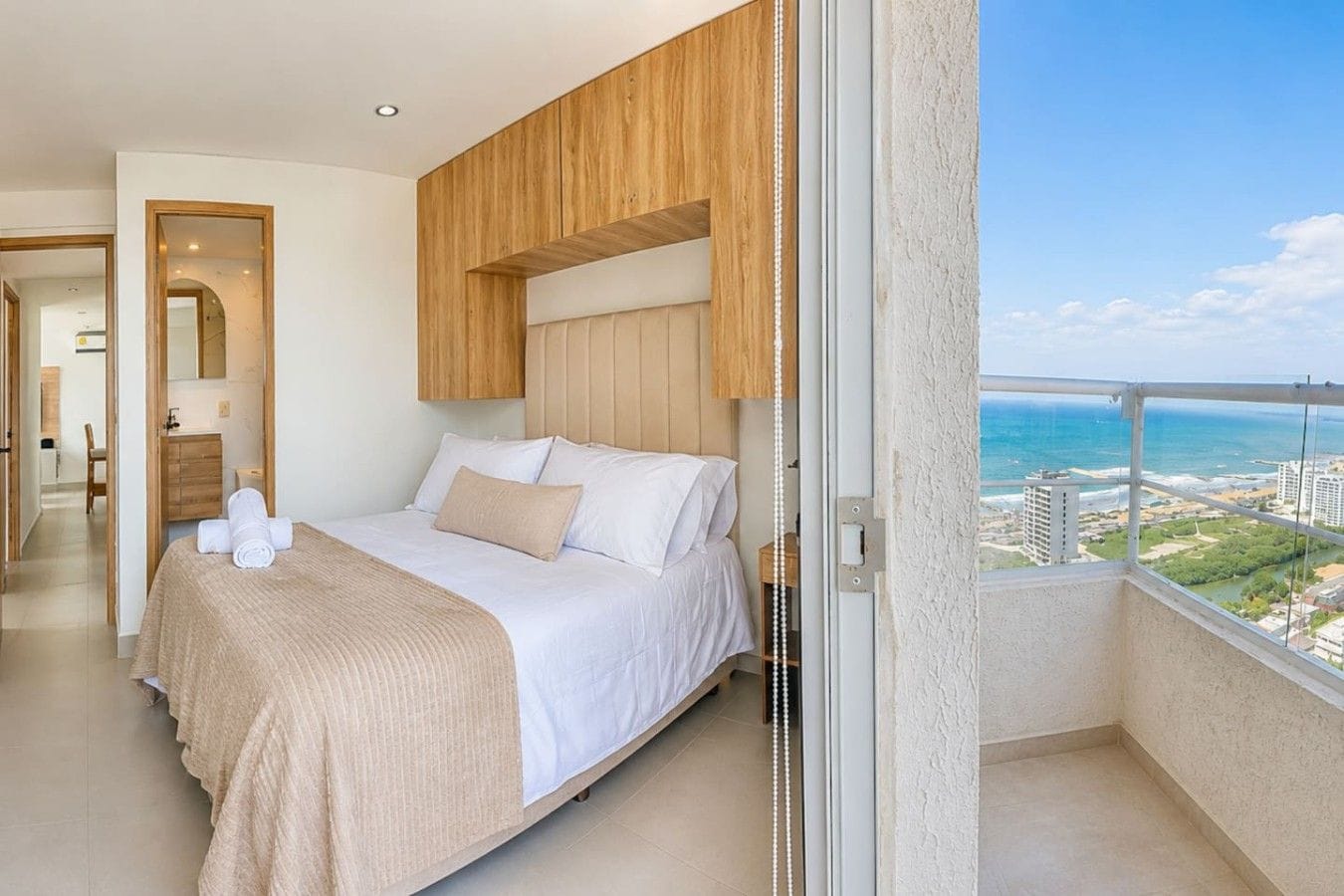 A hotel room with a bed, a bathroom, and a balcony with a view of the ocean.