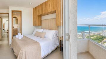 A hotel room with a bed, a bathroom, and a balcony with a view of the ocean.
