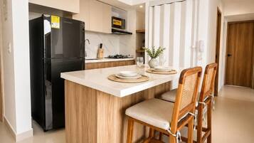 A modern kitchen with a central island, wooden chairs, and a black refrigerator.