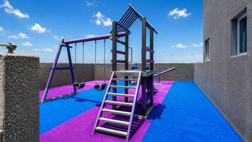Zona infantil con columpios, un tobogán y una escalera sobre un suelo azul y morado.