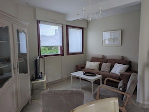 Een woonkamer met een bank, stoelen, een salontafel, een televisie en een radiator.