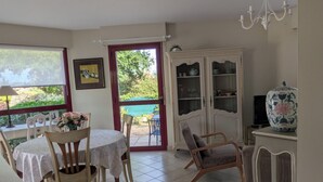 A dining area with a table and chairs, a cabinet with glass doors, and a view through a door to an outdoor area. - Heading to Vannes (Vannes)