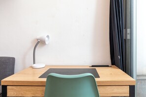 Une pièce avec un bureau en bois, une chaise verte, une lampe de bureau blanche et un tapis noir.