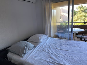 Une chambre d’hôtel avec un lit, une fenêtre avec des rideaux et une vue sur un balcon équipé de chaises et d’une table.